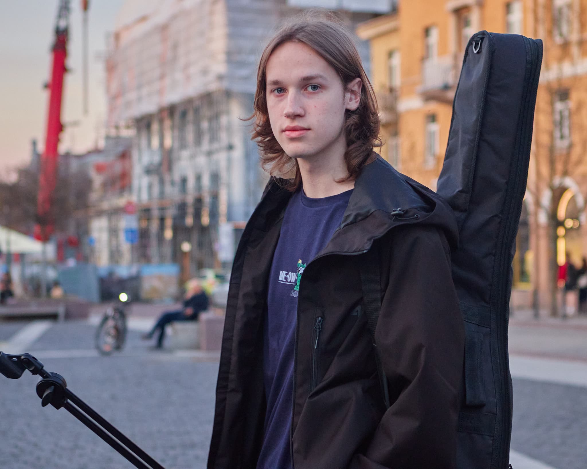Muzikanto portretas mieste Jaunas vyras su gitaros dėklu pozuoja miesto fone